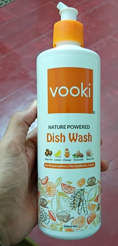 Customer's hand holding a white bottle of Vooki Nature Powered Dish Wash with an orange pump top.