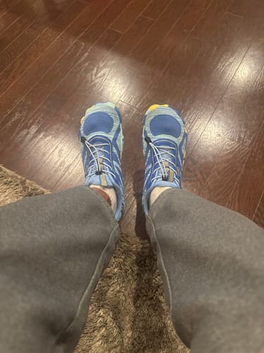 Reviewer looking down at their blue athletic toe shoes on a wood floor.