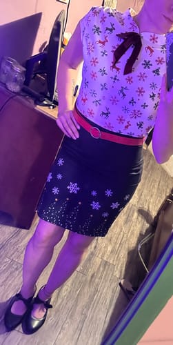Customer posing in the 1960s Christmas Pencil Dress. The festive dress features a printed top, black skirt, and red belt.