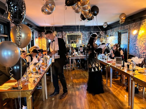 Customers dressed in 1920s outfits for a party, playing the Murder Mystery Game Kit at decorated long tables.