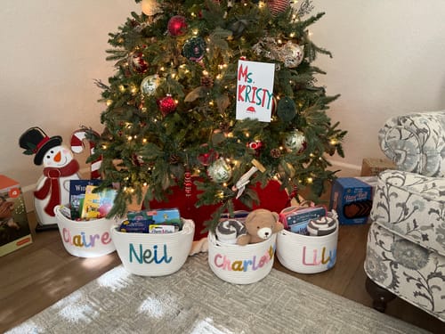 Reviewer's four personalized knitted baskets filled with gifts and books, placed under a Christmas tree.