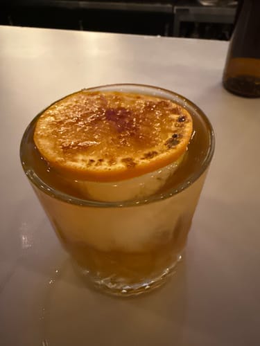 Close-up of a reviewer's Old Fashioned made with Sweet Potato Syrup and garnished with a caramelized orange slice.