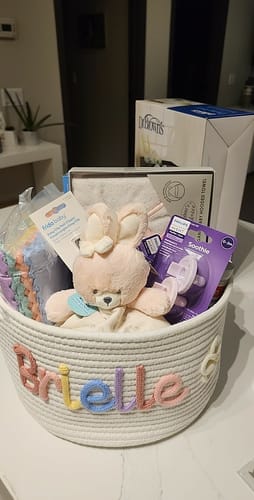 Customer's personalized white basket with 'Brielle' knitted in multicolor yarn and filled with baby essentials.
