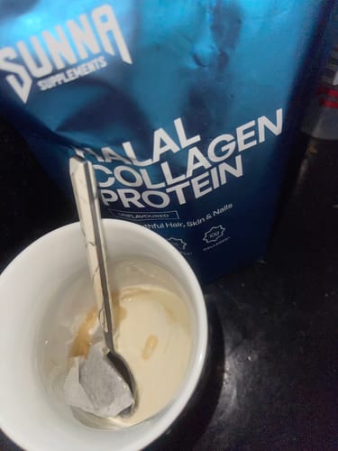Customer's Halal Collagen Protein bag behind a white mug containing a spoon and a teabag in a creamy liquid.