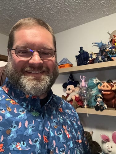 Customer smiling while wearing the blue 'Stitch Being Stitch' short sleeve shirt in front of Disney collectibles.