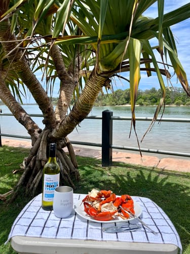 Customer's white Travel Wine Tumbler on an outdoor table with a bottle of wine and a plate of crab.