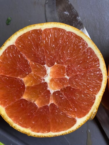Rezensent zeigt das roséfarbene, saftige Fruchtfleisch einer halbierten Cara Cara Orange.