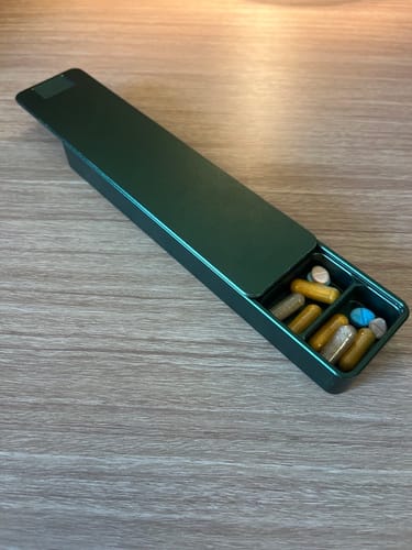 Customer's open, dark green Nano Case on a wooden surface, filled with assorted pills and vitamins.