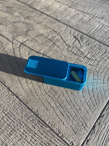 Customer's open blue Nano Case with one capsule inside, shown on a wood-grain surface.