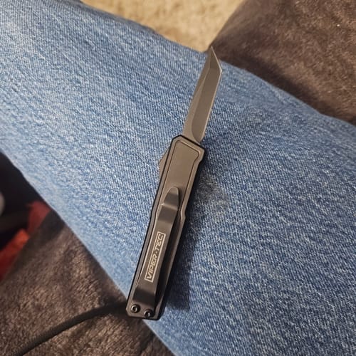 Customer's black VT Black Widow Mini OTF Knife with the blade extended, resting on a person's leg.