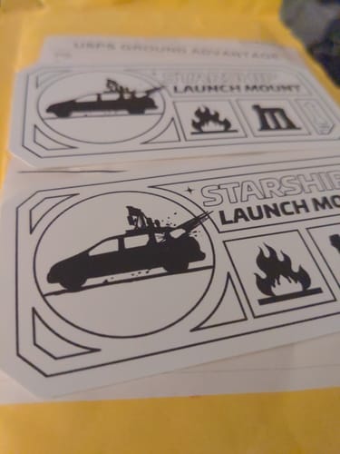 Customer's two black and white Original Launch Mount stickers resting on a yellow surface.