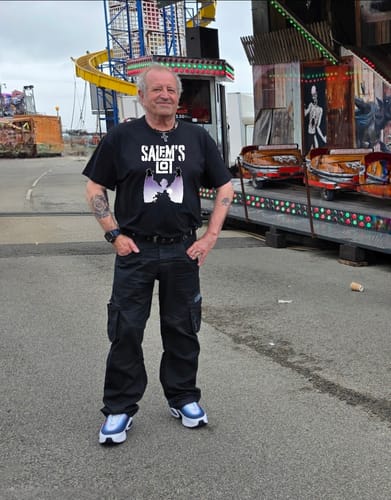 Reviewer wearing the black unisex t-shirt with a large graphic print while standing at a fairground.