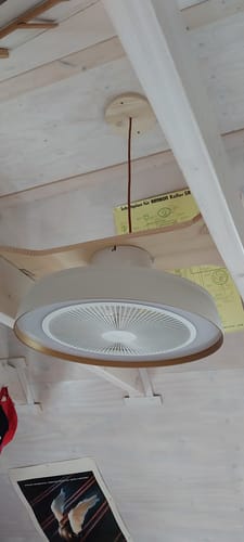 Rezensent zeigt den weißen OSRAM Deckenventilator, der mit einer speziellen Halterung an einer Holzdecke montiert ist.