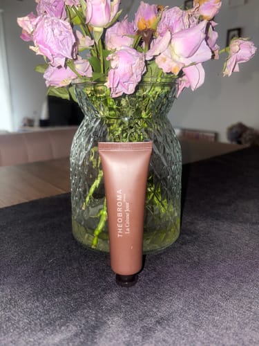 Photo d'un client montrant le tube de La Crème Jour posé devant un vase de roses.