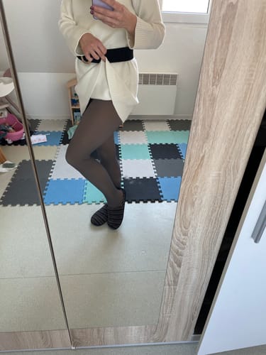 Cliente portant le collant polaire LEGGS avec une robe pull blanche dans un miroir.