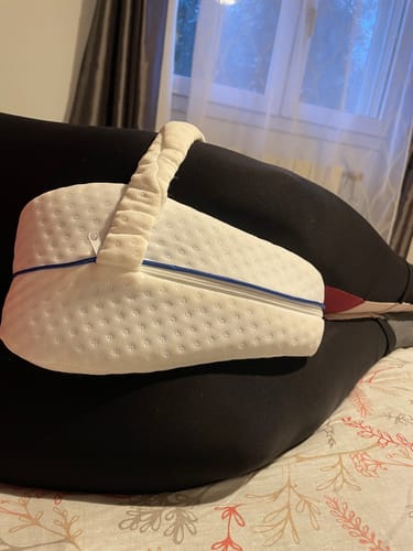 Cliente utilisant le coussin genoux blanc avec sa lanière de maintien, positionné entre ses jambes.