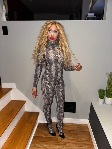 Reviewer standing on stairs, wearing the form-fitting Naked Print Jumpsuit in a snakeskin pattern with black heels.