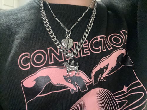 Reviewer wearing the Cosmic Heart Pendant layered with another silver chain necklace over a black sweater.