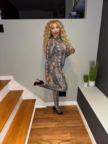 Reviewer posing in the full-footed Naked Print Jumpsuit, lifting one leg to show the fit with a black stiletto.