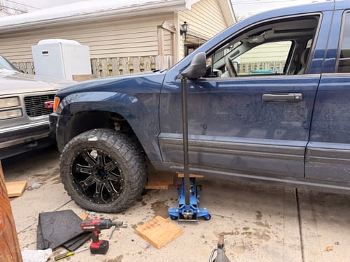 Customer's dark blue Jeep jacked up while installing 2" wheel spacers, showing the new black rim mounted.