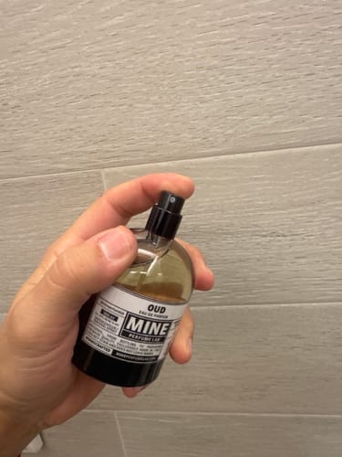 Un recensore tiene in mano la boccetta di profumo OUD, pronto a spruzzare.
