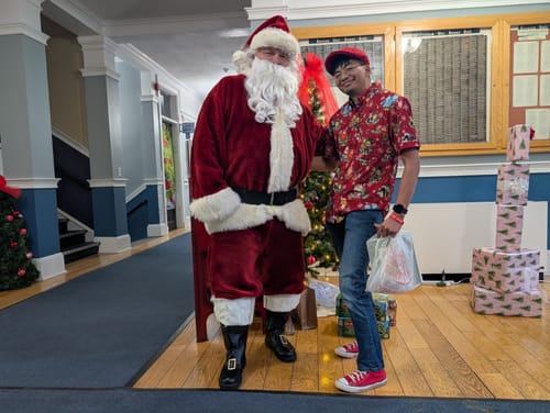 Reviewer wearing the red 'Feels Like Christmas' shirt while smiling and posing next to Santa Claus.