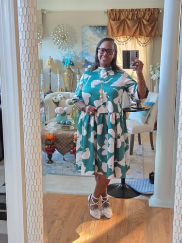 Reviewer taking a mirror selfie while wearing the green and white floral high neck midi dress indoors.