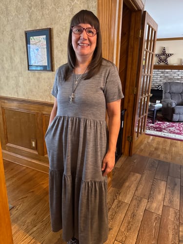 Reviewer standing indoors wearing the ankle-length, grey Lucia Dress with her hand in a side pocket.