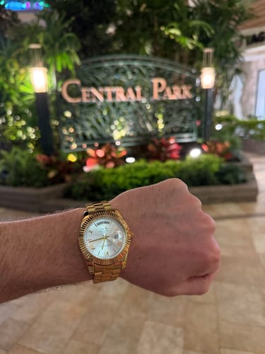 Close-up on a reviewer's wrist showing the gold Lucky Fours® Santos watch with a white dial.