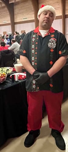 Customer wearing the black El Sancho Clause Guayabera shirt with a Santa hat at an event.
