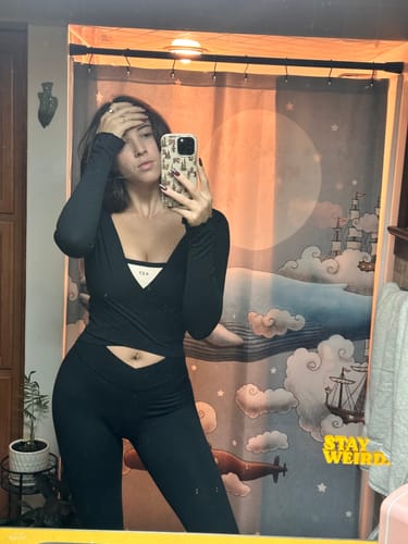 Reviewer in a mirror selfie, wearing the cream and black Micro Bra layered under a black long-sleeved top.