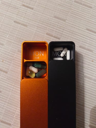 Customer's close-up of the orange and black Weekly AM-PM Vitamin Case 2.0, open to the 'MON' compartments filled with pills.