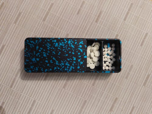 Reviewer's black and blue Mission Case open on a table, showing two compartments filled with pills.