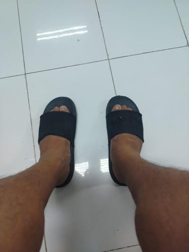 Customer's feet wearing the black Nike Men's Offcourt Slides on a white tiled floor.
