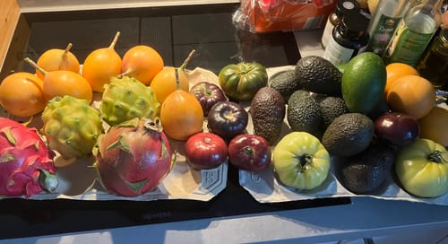 Rezensent zeigt die frischen Avocados und verschiedenfarbigen Tomaten aus der Box auf einer Küchentheke.