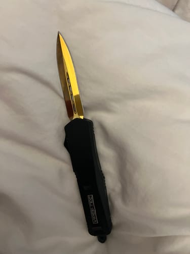 A reviewer's Black Ghost OTF Knife with its beautiful gold blade extended from the sleek black handle.