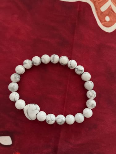 Customer's white and grey marbled crystal bead bracelet with a heart-shaped bead, on a red surface.