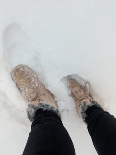 Customer wearing the Rise I Winter Barefoot Boots with dark faux fur collars, standing in snow.
