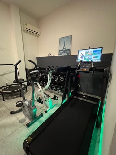 Rezensent zeigt sein schwarzes Jet-Laufband mit großem, eingeschaltetem Bildschirm in einem Heim-Fitnessstudio.