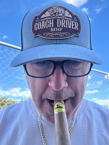 Customer wearing a blue and black Bison Custom Hat with a personalized 'Coach Driver' leather patch.