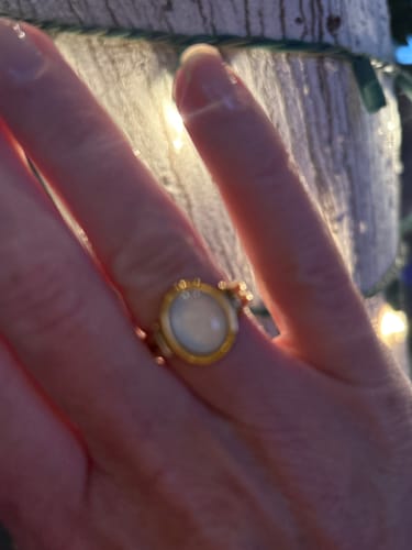 Close-up of a reviewer wearing the gold Kai Mother Of Pearl ring on their finger in a warmly lit setting.
