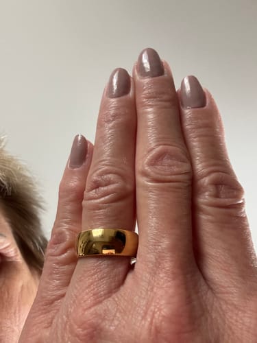 Customer's hand wearing the wide, 8mm Elyos ring, showing its shiny gold finish.