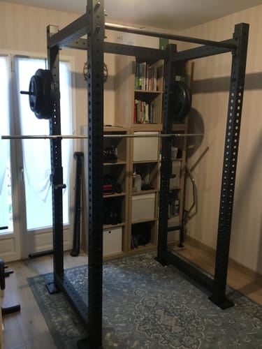 Ein Kunde zeigt das schwarze R8 Base 1 Power Rack, das in einem kompakten Heim-Fitnessstudio aufgebaut ist.