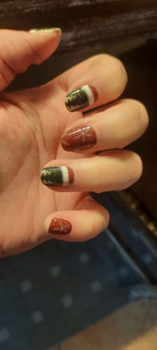 Nahaufnahme der Hand einer Rezensentin, die eine Maniküre mit den "Santa's Village"-Nagelfolien auf kurzen Nägeln zeigt.
