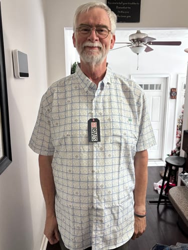 A customer smiles while wearing The Scorekeeper short sleeve shirt, showing its scorecard-style grid pattern.