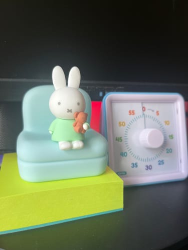 Customer's Miffy Sofa Phone Stand on a desk. Miffy sits on a light-blue sofa in a green dress, holding a teddy bear.