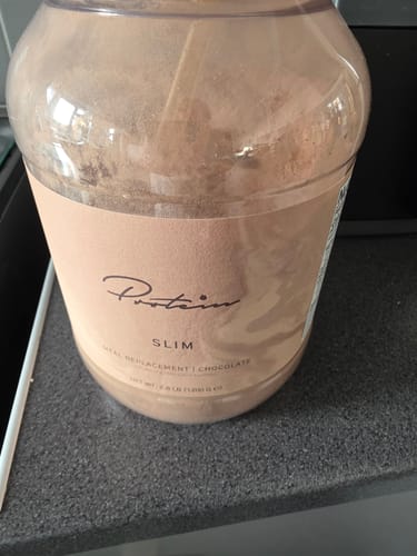 A customer's large jar of Chocolate Slim Meal Replacement powder resting on a kitchen counter.