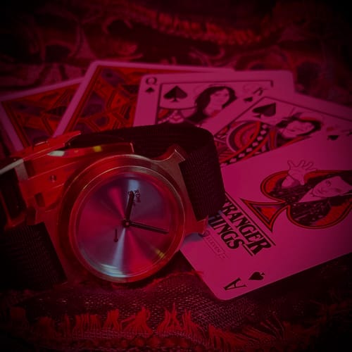 A customer's Stranger Things playing cards arranged with a watch in a stylized, red-lit scene.