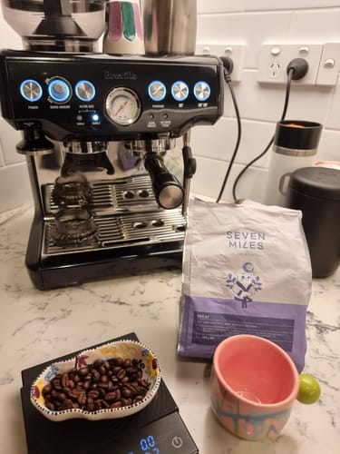 Customer's bag of Decaf Coffee on a kitchen counter next to an espresso machine and a bowl of whole beans.