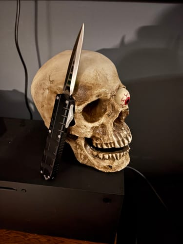 Customer's black Triton OTF knife with the blade extended, resting against a decorative skull.